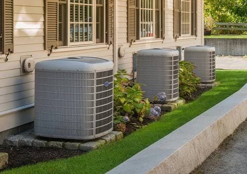 Three outdoor condenser units installed beside a home